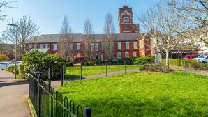 A red brick building with a clock tower, surrounded by a green lawn and a black fence.