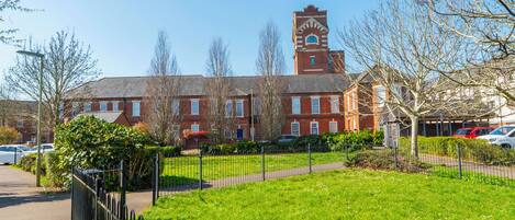 A red brick building with a clock tower, surrounded by a green lawn and a black fence.