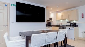 A modern kitchen with a flat-screen TV, a dining table with chairs, and a coffee machine.