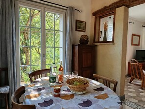 A dining area with a table set for two, featuring a bottle of water, a bottle of wine, a glass, a basket of fruit, and a jar of jam.