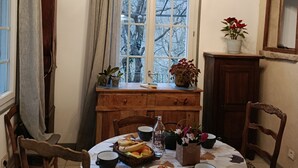 A dining area with a round table, chairs, a chandelier, a window with curtains, a painting, and a wooden cabinet. - Charming gîte with swimming pool south Ardèche L'Oustal (Vesseaux)