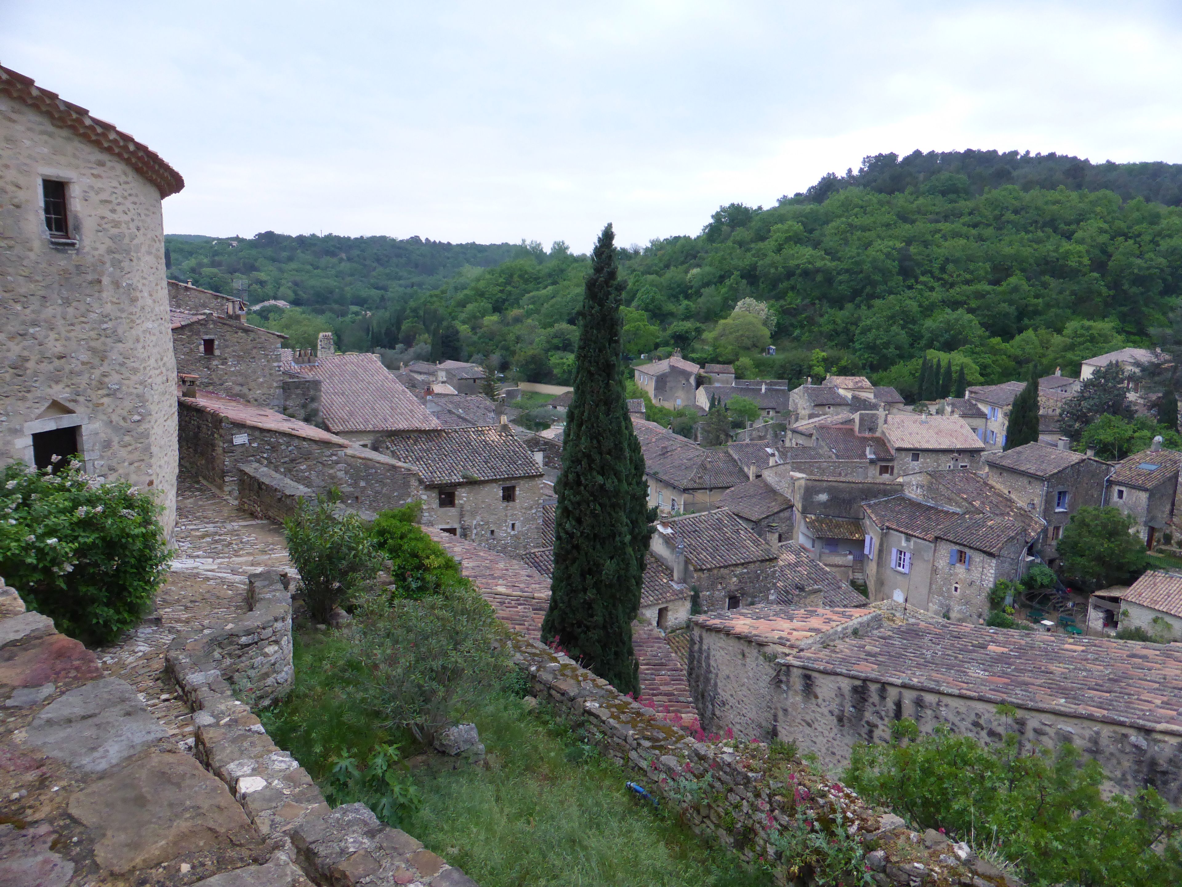 Un pueblo histórico con edificios de piedra, calles estrechas y un ciprés destacado.