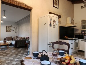 A cozy living room with a sofa, a dining table with chairs, a kitchen area with a stove, and a refrigerator. - Charming gîte with swimming pool south Ardèche L'Oustal (Vesseaux)