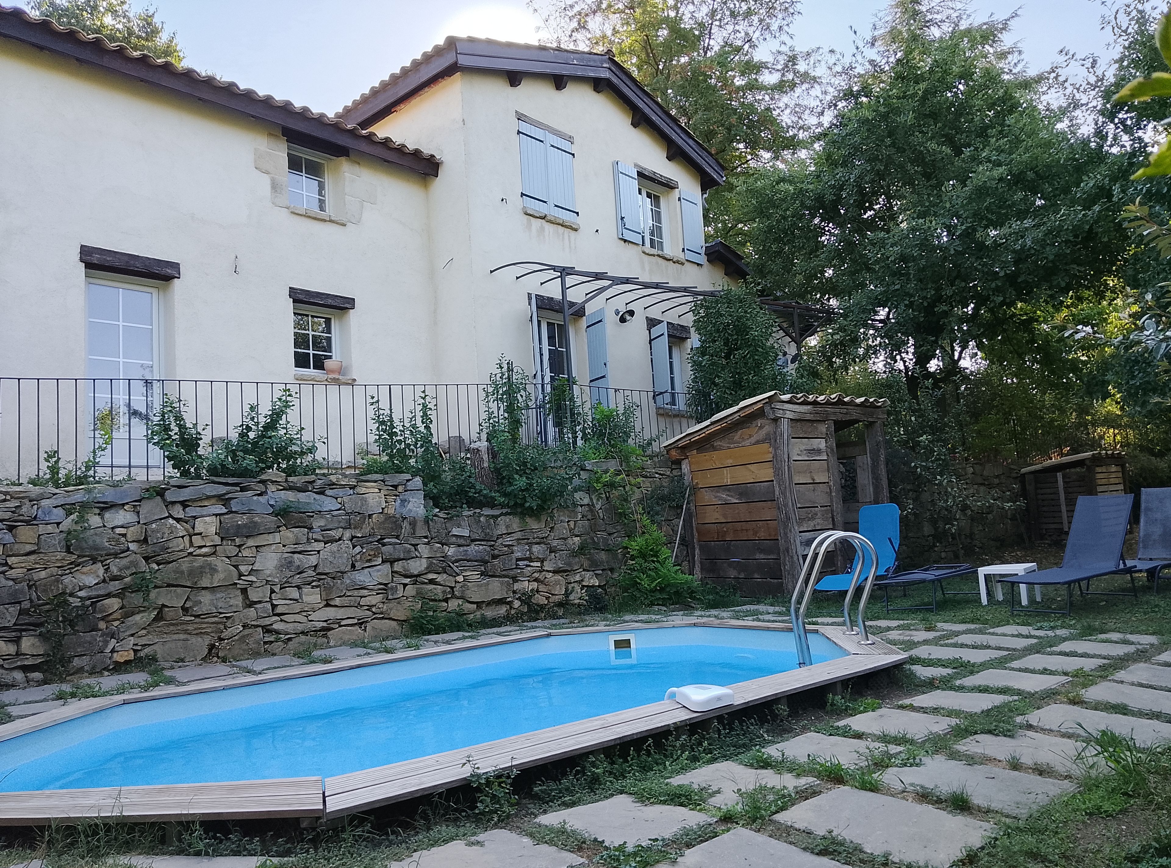 Ein Schwimmbecken mit Holzterrasse, Steinmauer und Holzschuppen.