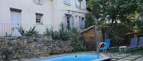 Una piscina con muelle de madera, pared de piedra y cobertizo de madera.