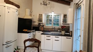 A kitchen with white cabinets, a black countertop, a stove, a sink, and a window with a view of greenery outside. - Charming gîte with swimming pool south Ardèche L'Oustal (Vesseaux)