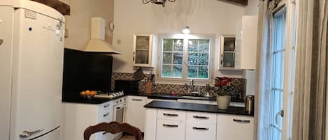 A kitchen with white cabinets, a black countertop, a stove, a sink, and a window with a view of greenery outside.