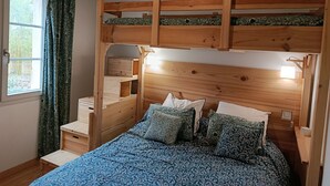 A bunk bed with a wooden headboard, a window with curtains, and a patterned bedspread. - Charming gîte with swimming pool south Ardèche L'Oustal (Vesseaux)