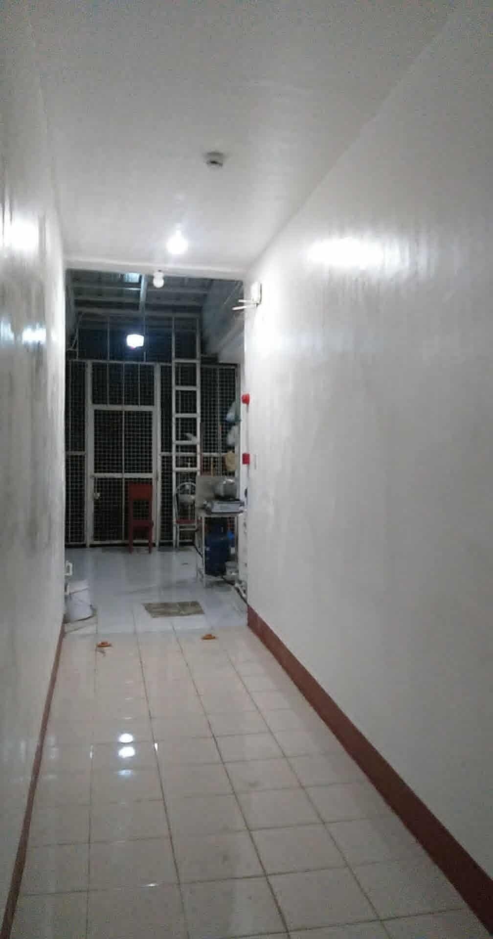 Un pasillo con suelo de baldosas, paredes blancas y una reja metálica al final.