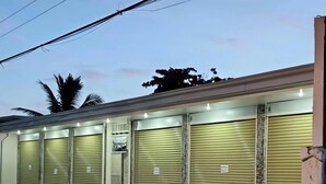 A building with multiple closed shuttered storefronts, a gated entrance, and a paved ground.