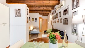Ein Zimmer mit Holzboden, einem Esstisch mit Blumenvase, einer Weinflasche und einem Sofa.