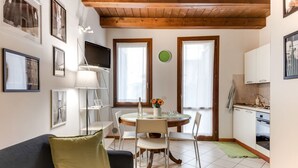 Ein Wohnzimmer mit einer Couch, einem Esstisch, Stühlen, einem Fernseher und einer Küchenzeile mit Schränken und einer Spüle.