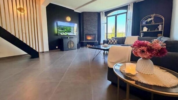 A modern living room with a fireplace, a TV mounted on the wall, a staircase, and a round table with a vase of flowers. - House with pool and jacuzzi in Cagnes-sur-Mer (Cagnes-sur-Mer)