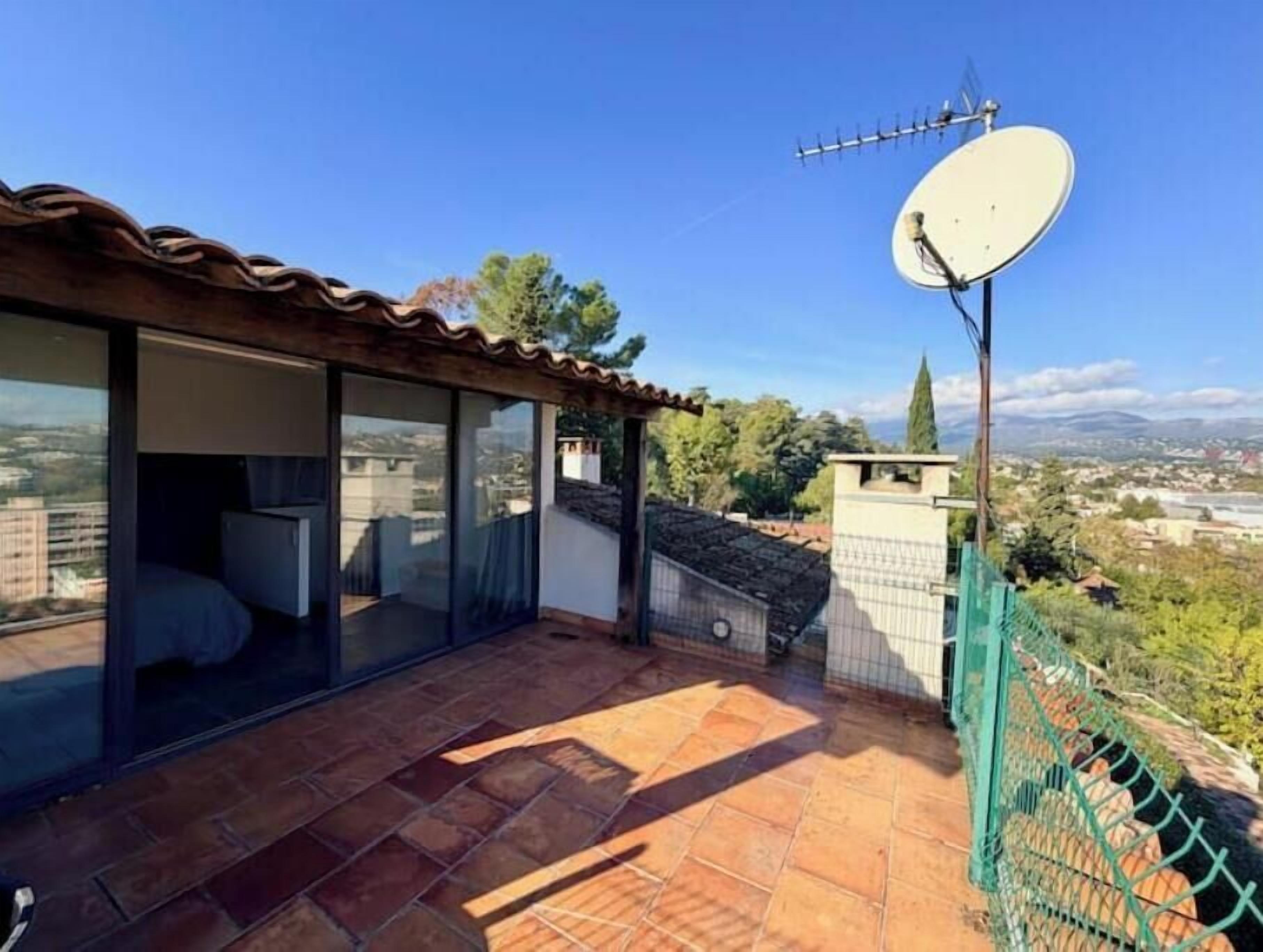 Un balcon doté d’une antenne parabolique, de portes vitrées et offrant une vue sur le paysage urbain.