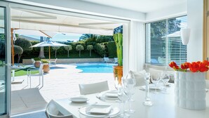A dining area with a pool view, white furniture, and a vase of red tulips. - Beautiful villa between Nice and Cannes (Villeneuve Loubet)