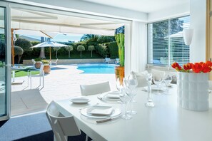 Ein Essbereich mit Blick auf einen Pool, mit weißer Möbel und einer Vase mit roten Tulpen.