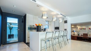 A modern kitchen with a central island, bar stools, pendant lighting, and a view through a glass door. - Beautiful villa between Nice and Cannes (Villeneuve Loubet)