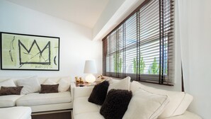 A modern living room with a white sofa, a framed artwork, a lamp, and a window with blinds. - Beautiful villa between Nice and Cannes (Villeneuve Loubet)