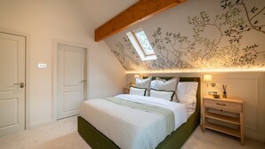 A bedroom with a sloped ceiling, a skylight, a bed with multiple pillows, a nightstand, and a wall with a tree mural. - Luxury Golf House near Royal Birkdale (The Open) | Hot Tub | Sleeps 12+ (Southport)