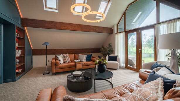 A spacious living room with a leather sofa, a coffee table, and a side table. There is a bookshelf and a large window providing natural light. - Luxury Golf House near Royal Birkdale (The Open) | Hot Tub | Sleeps 12+ (Southport)