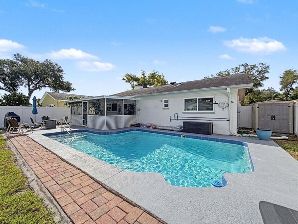 Ein Garten mit Schwimmbecken, überdachter Terrasse und umzäunter Grundstück.