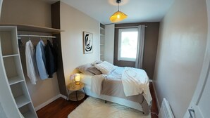 Et soveværelse med seng, et natbord med lampe, et garderobeskab, et vindue og en loftslampe.
