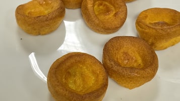 Une assiette de « Yorkshire puddings » sur une assiette blanche, avec un pot de confiture de framboises et un récipient en plastique en arrière-plan.