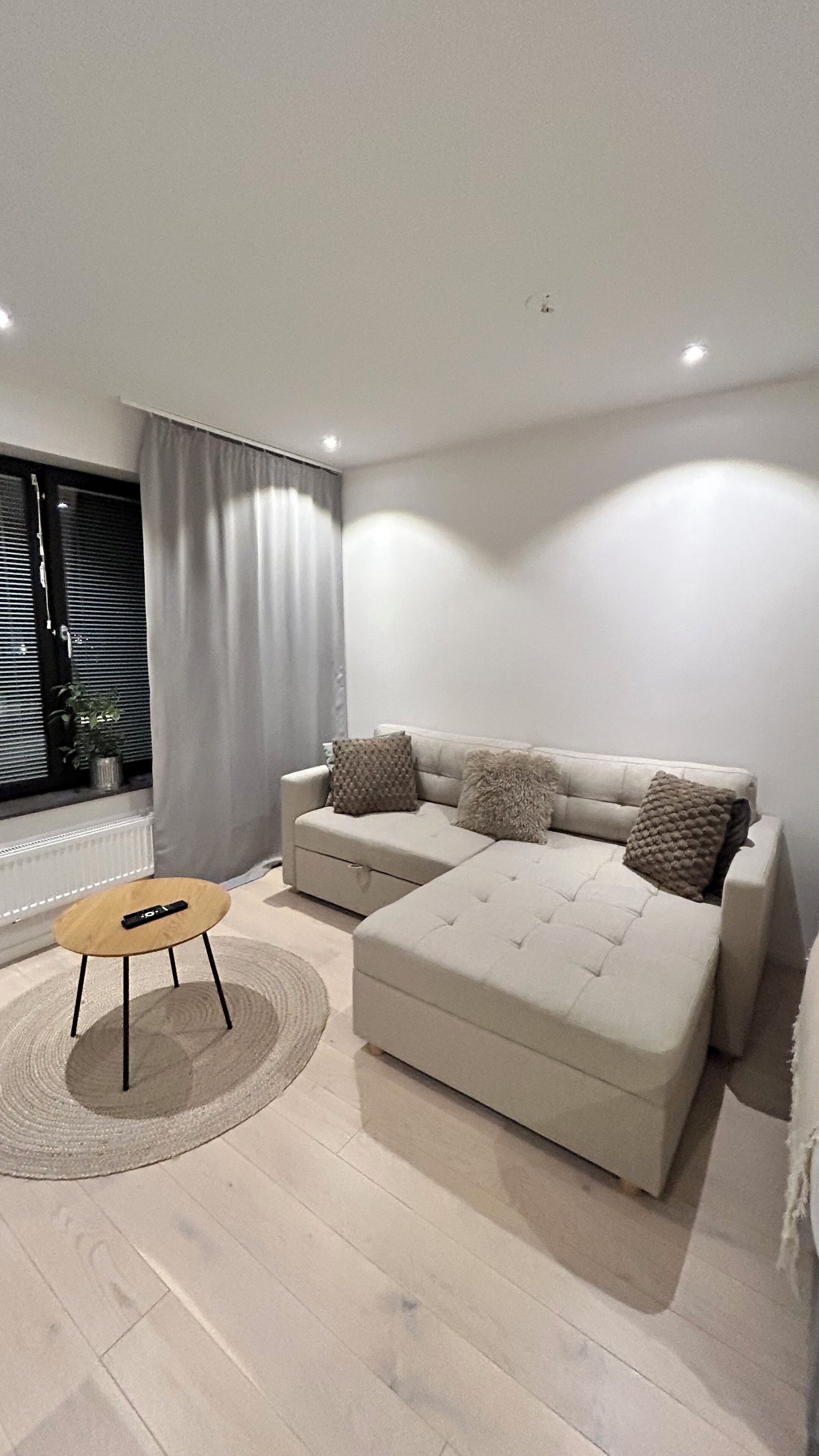 A modern living room with a sofa, a small round table, and a window with curtains.