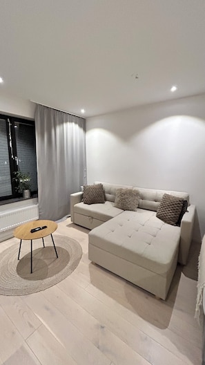 A modern living room with a sofa, a small round table, and a window with curtains.