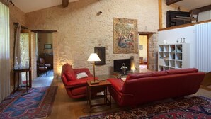 A cozy living room with a stone wall, red leather sofas, a fireplace, and a bookshelf.