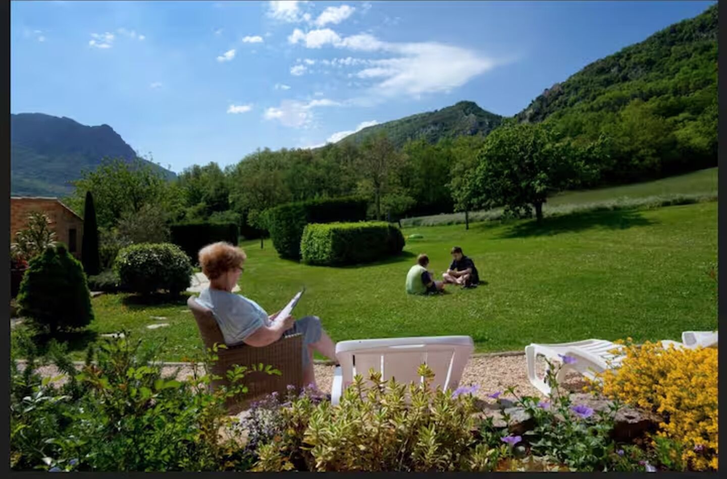 En trädgård med en gräsmatta, en byggnad och ett berg i bakgrunden.