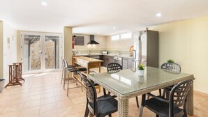 A spacious kitchen with a dining area, featuring a glass-top table, wicker chairs, and a built-in refrigerator.