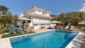 A poolside view of a two-story house with a swimming pool, lounge chairs, and a patio area.