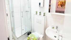 Une salle de bain avec une douche à parois de verre, des toilettes dotées d’un abattant décoré de motifs floraux et un lavabo avec un miroir au-dessus.