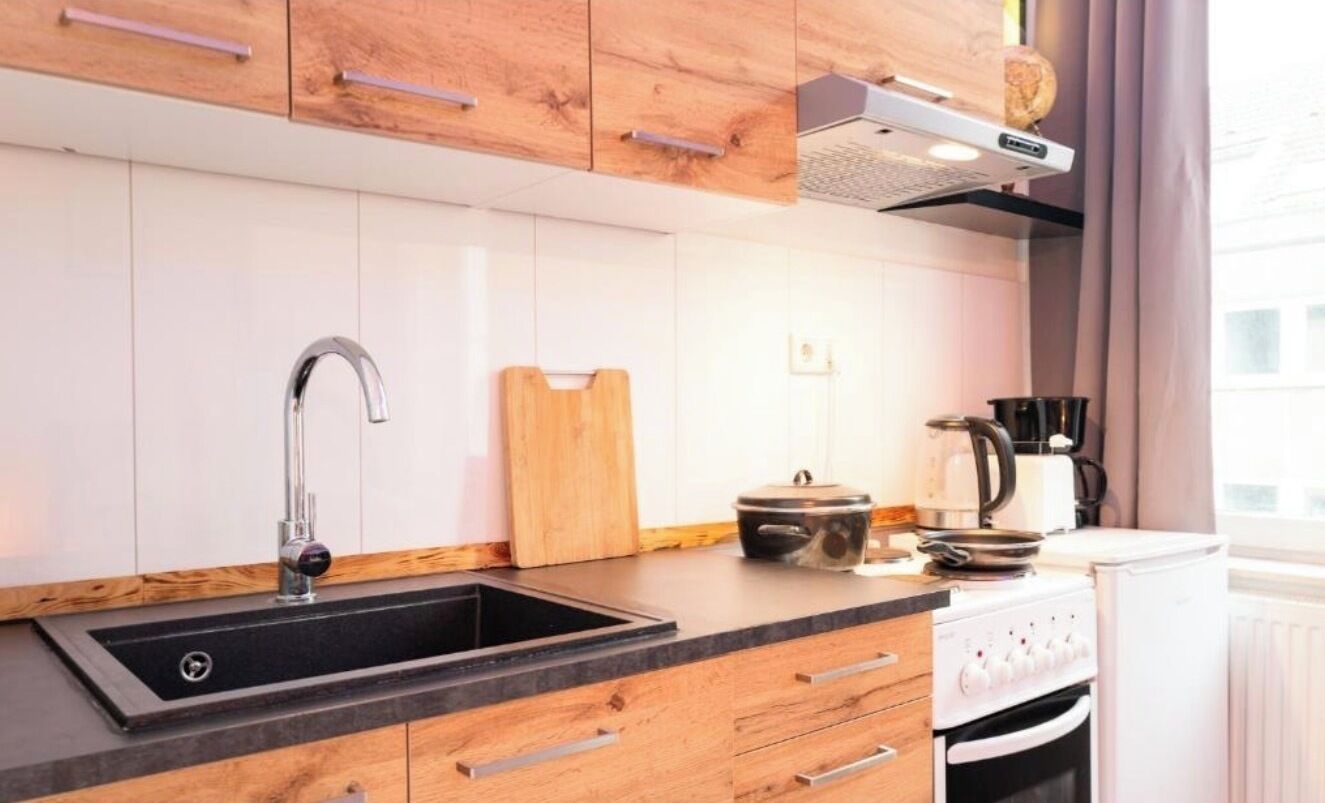 Eine moderne Küche mit Spüle in Schwarz, Holzschränken, Schneidebrett, einem Slow Cooker und einer Kaffeemaschine.