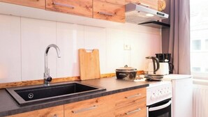 Une cuisine moderne avec un évier noir, des meubles en bois, une planche à découper, un autocuiseur et une machine à café.