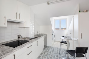 Une cuisine moderne avec des meubles blancs, une plaque de cuisson à induction noire et une fenêtre donnant sur un paysage urbain.