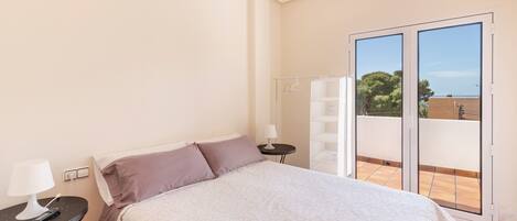 A bedroom with a bed, a nightstand, a lamp, and a view of a balcony with a railing.