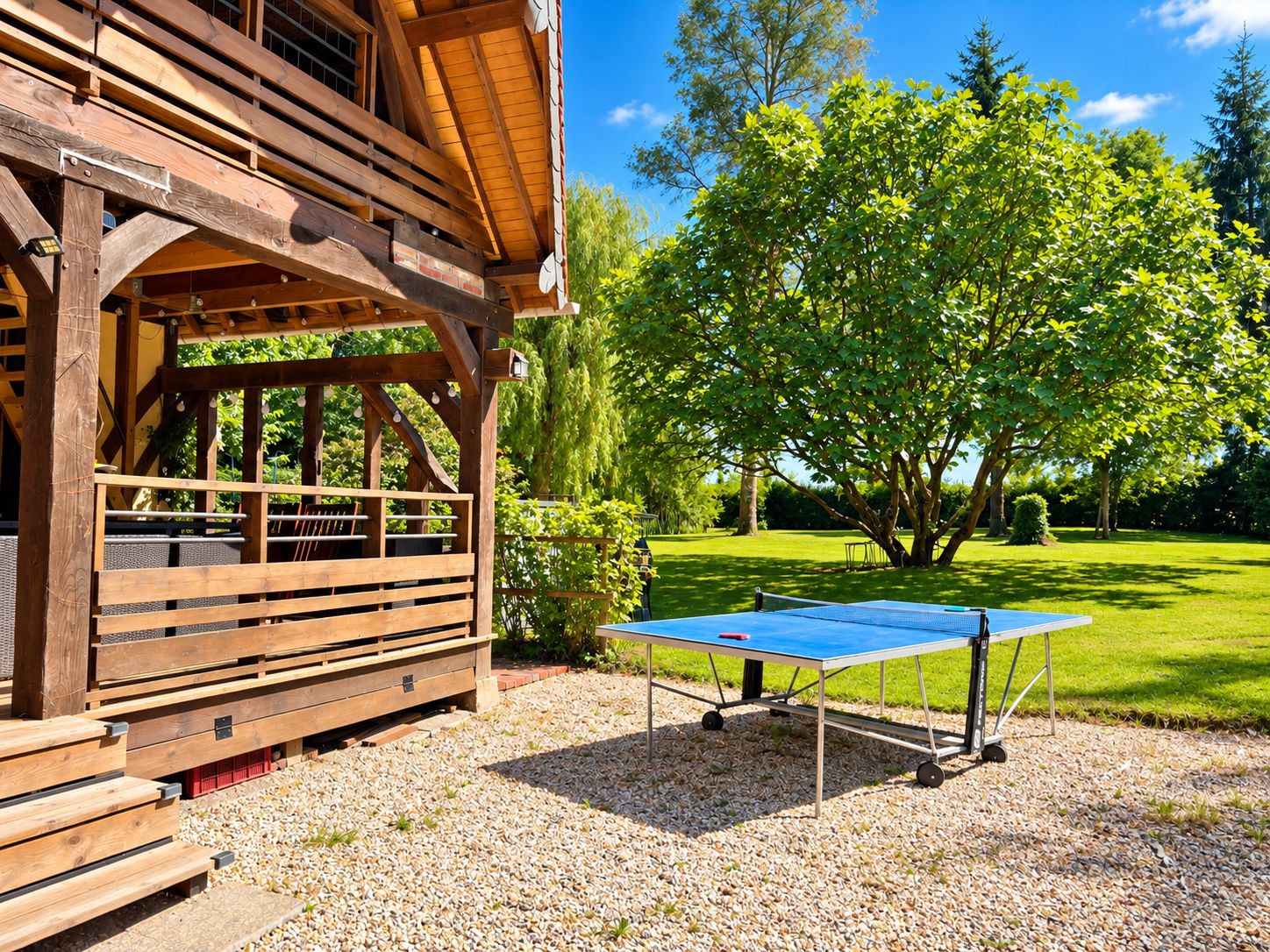 Un espacio al aire libre con piso de madera, una mesa de ping pong, bancos y una zona de estar techada.