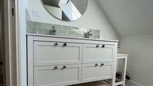 A bathroom with a white vanity, a round mirror, and a tiled backsplash. - 3 bedroom house and garden facing the beach. Arzon. Gulf of Morbihan (Arzon)