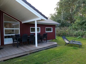 Um deck de madeira com móveis de exterior, um alpendre coberto e um jardim com uma espreguiçadeira.