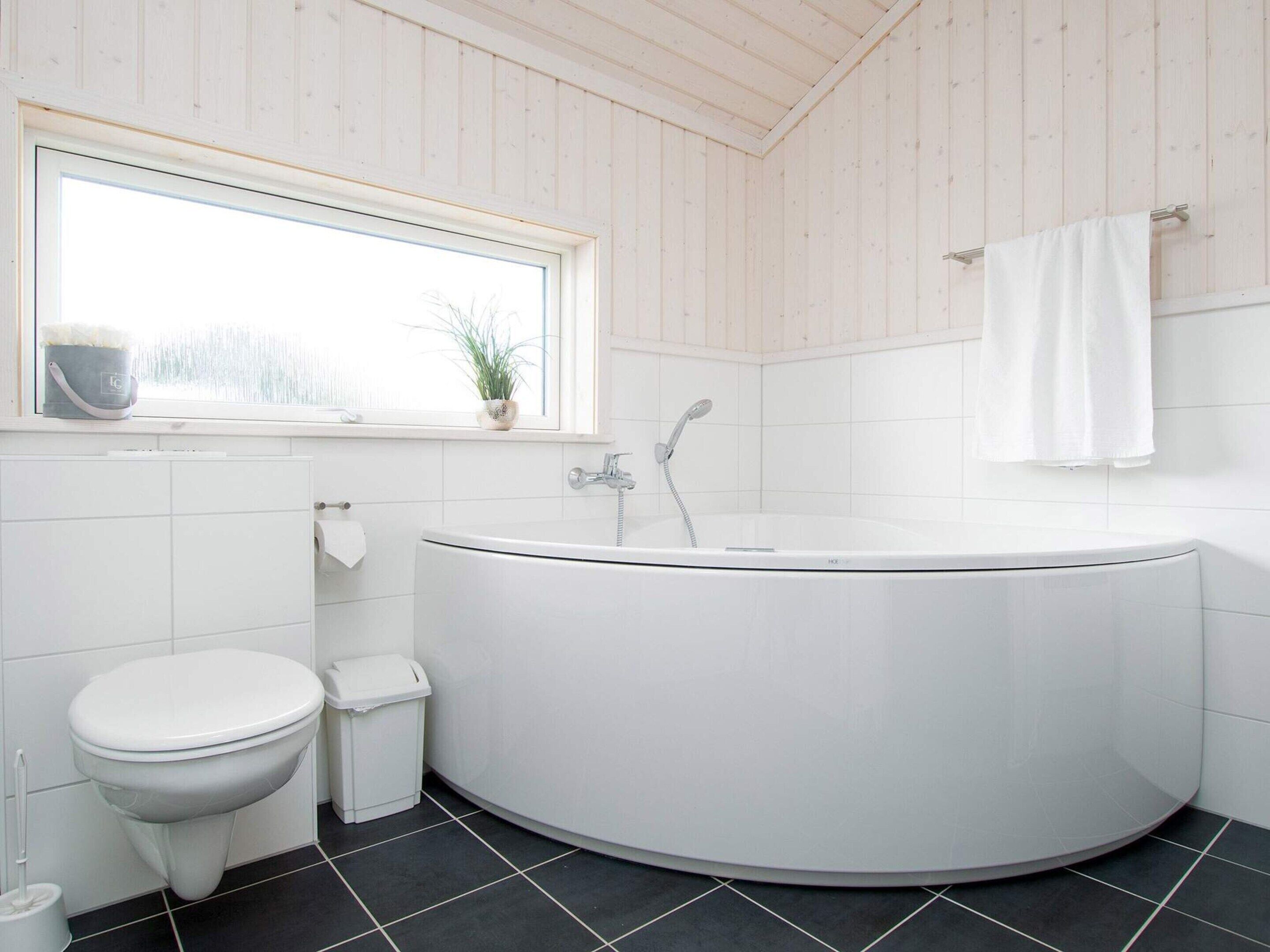 A modern bathroom with a freestanding bathtub, a toilet, and a window with a view.
