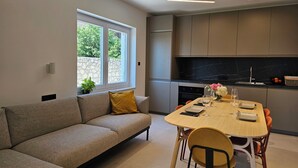 A modern kitchen with a built-in oven, a dining table with chairs, and a sofa in a living area with a window. - Modern vacation apartment in Crikvenica with internet, sea view, barbecue (Crikvenica)