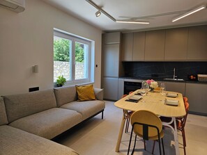Eine moderne Küche mit Einbauofen, einem Esstisch mit Stühlen und einer Couch in einem Wohnbereich mit Fenster.