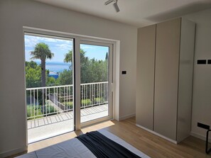 Ein Schlafzimmer mit einer großen Glasschiebetür, die auf einen Balkon führt, einem Bett und einem Kleiderschrank.