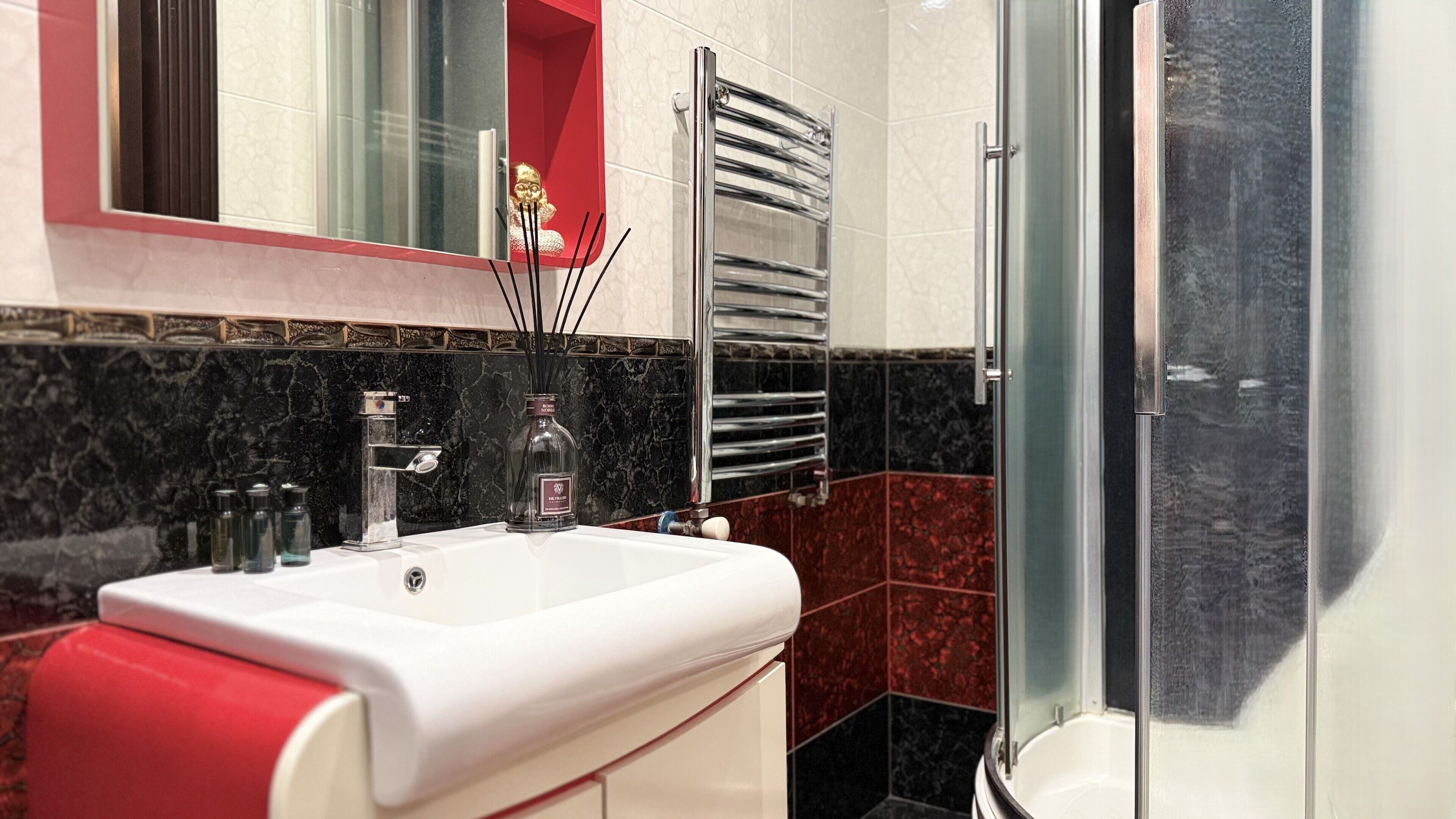 Un baño con un lavamanos blanco, un espejo, un perchero para toallas y una zona de ducha.