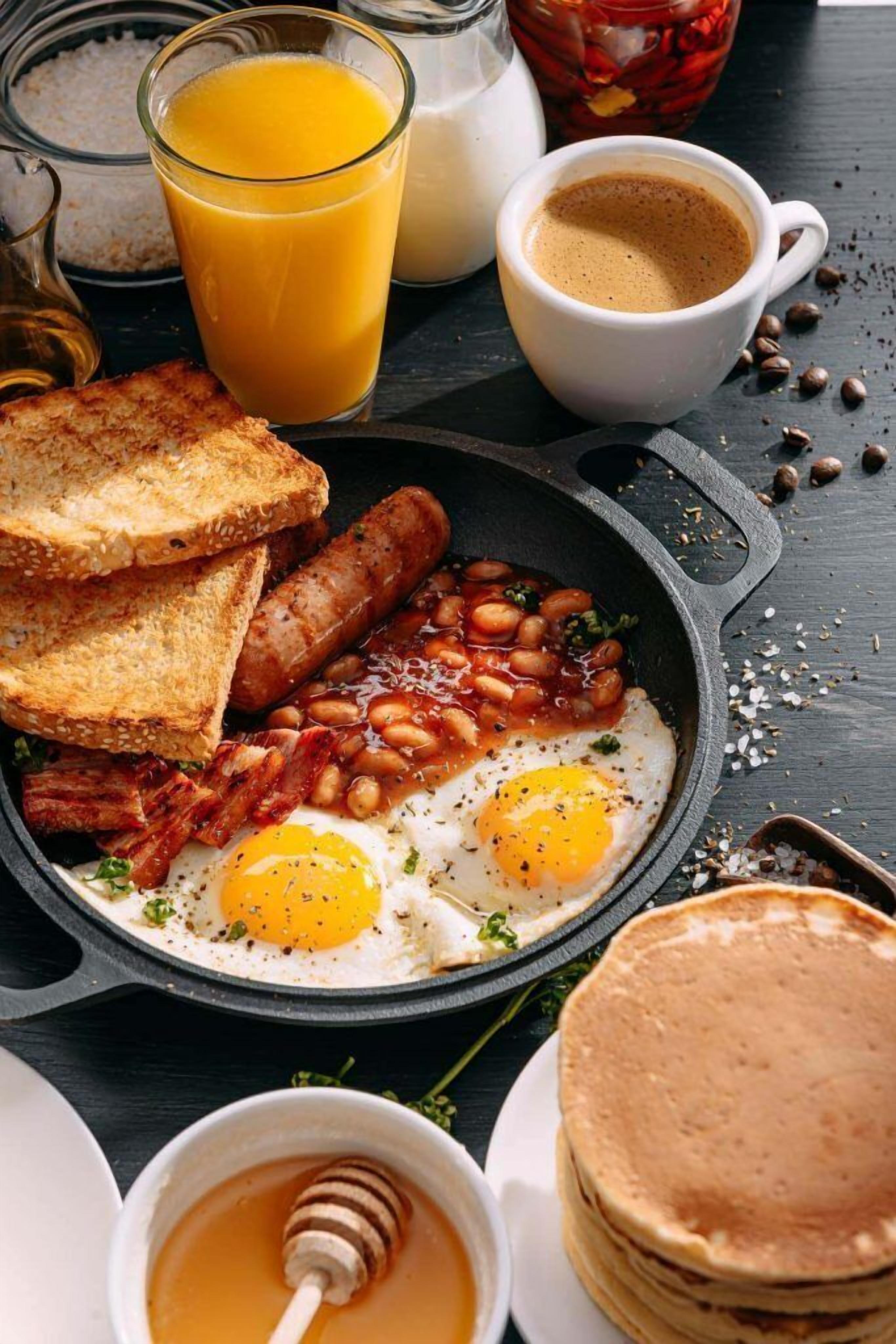 A breakfast plate with eggs, beans, bacon, toast, and pancakes.