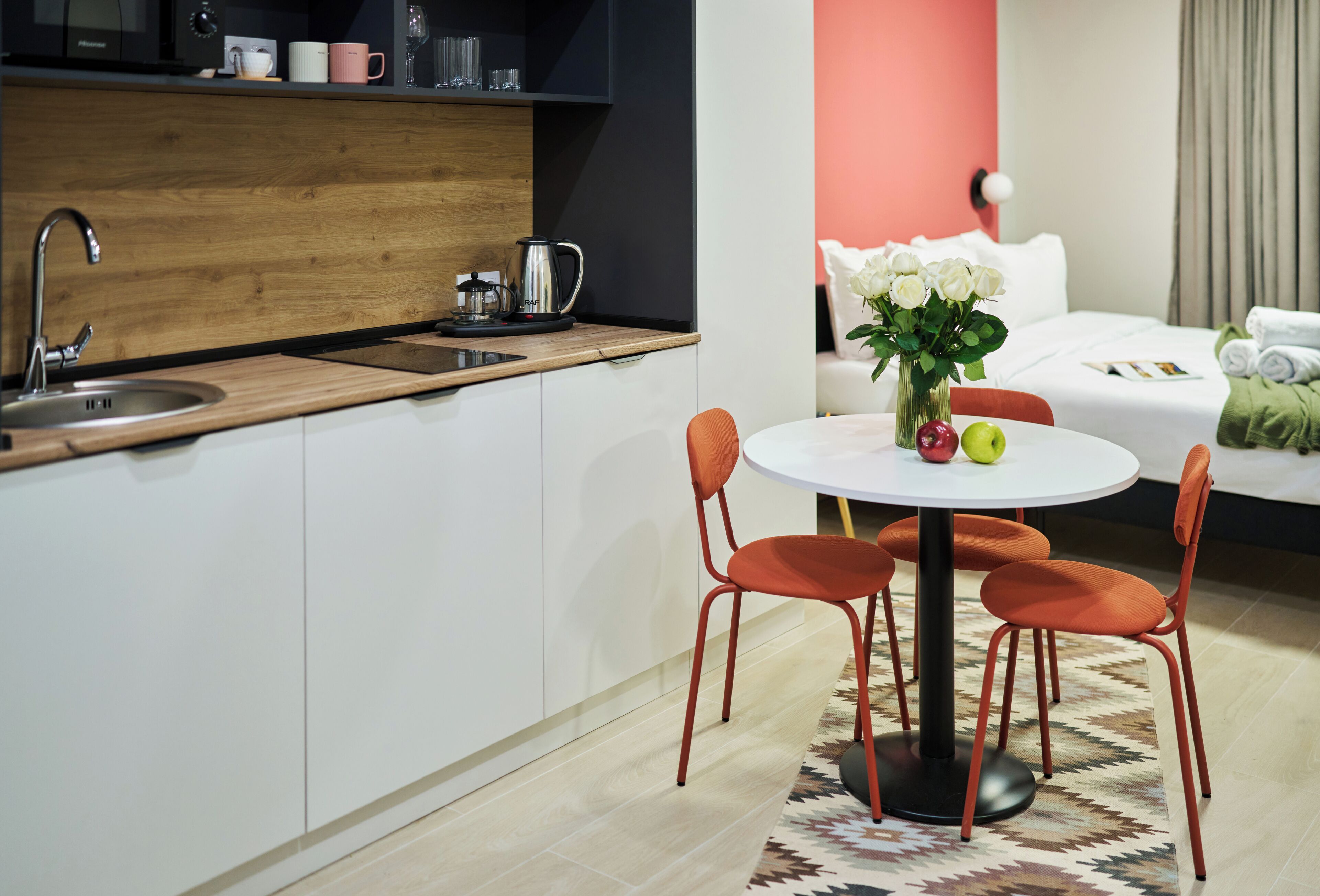 Una cocina moderna con un lavamanos, una cafetera y un comedor con una mesa redonda y sillas color naranja.