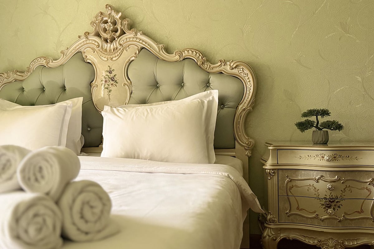 Ein Schlafzimmer mit einer gesteppten Kopfstütze, einem Bett mit weißer Bettwäsche, einem Nachttisch mit einer Vase und einer Wand mit einem Blumenmuster.