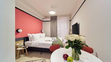 Una habitación de hotel con una cama, una mesa con manzanas y flores, un televisor y una pared roja.